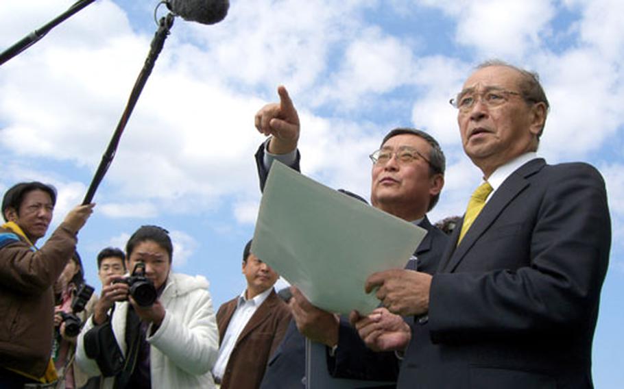 Reiji Fumoto, center, the prefecture's counselor for military affairs, and Okinawa Gov. Hirokazu Naikaima respond to reporters' questions Tuesday during a break in their tour of U.S. Marine bases.