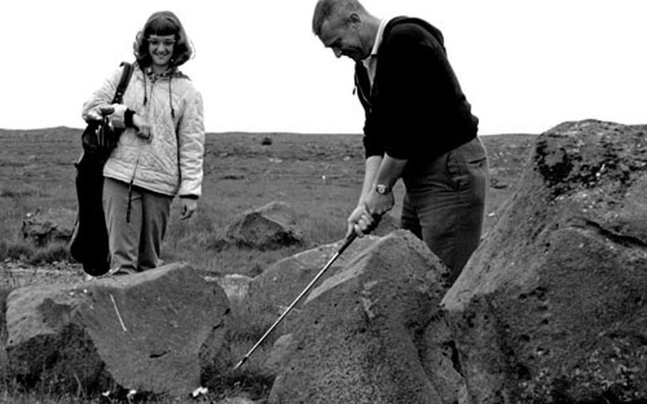 Caddy Sandy Emmert waits as CPO John E. Emert chips out from between some of Iceland's volcanic boulders.
