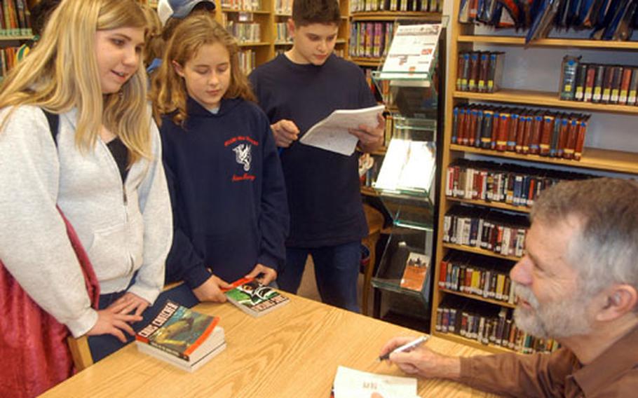 Author Chris Crutcher hands a signed book to Taryn Coullier at the library of Aviano Air Base in Italy on Tuesday. Crutcher, a popular author of books for young adults, visited with pupils at the high school and middle schools and signed dozens of books.