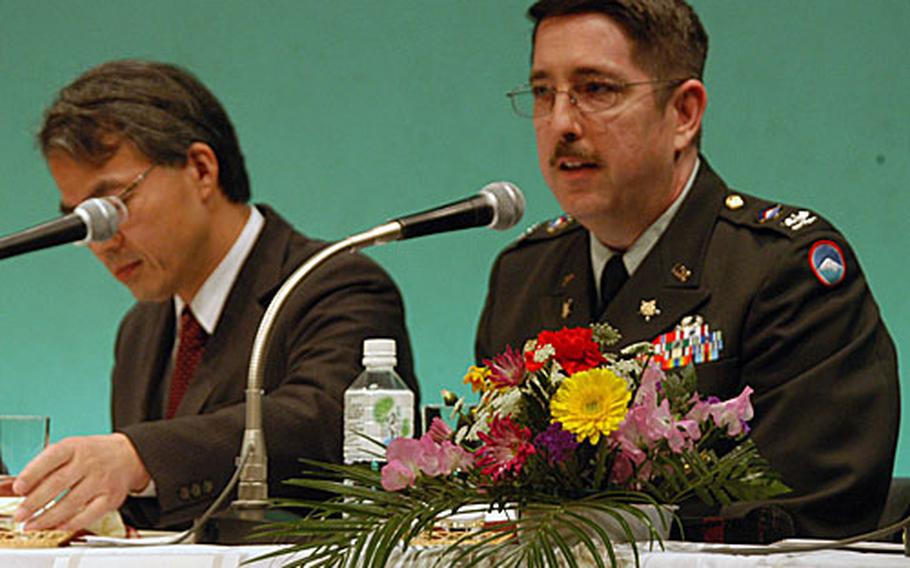Col. David Hunter-Chester, U.S. Army Japan deputy chief of staff for civil affairs, addresses a crowded auditorium in Sagamihara city on Saturday. On the left is Nobushige Takamizawa, Yokohama Defense Facilities Administration Bureau director, who also was a member of the panel.