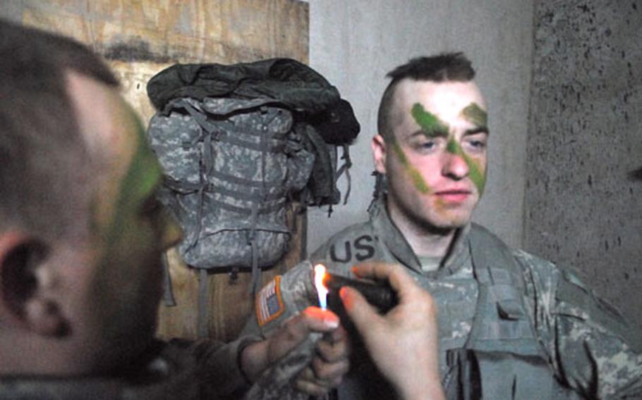 Pvt. George Maxham, 24, of Farmington, Maine, uses a cigarette lighter to apply camouflage face paint to Pvt. Andrew Ralston, of Eden Prairie, Minn., before a recent mission in downtown Ramadi.