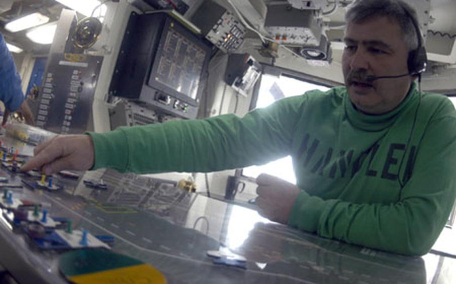 Lt. Cmdr. Doug Thornton, the "handler" or flight deck control officer, places shapes of aircraft on his "quigi board," mirroring the exact placement of real aircraft on the flight deck. The process, soon to be replaced by computers with touch-screens, provides a quick reference of the locations, fuel-level status, and availability of every one of the nearly 80 aircraft on the USS John C. Stennis.