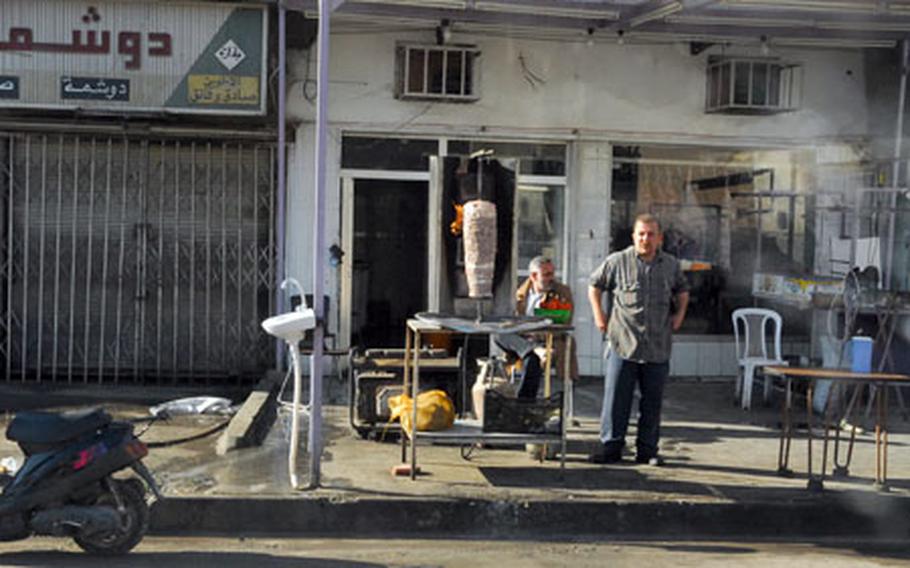 An Iraqi street vendor stands beside his shawarma stand and watches as a joint U.S. and Iraqi army patrol rolls past in eastern Baghdad's Zafaraniyah district recently.