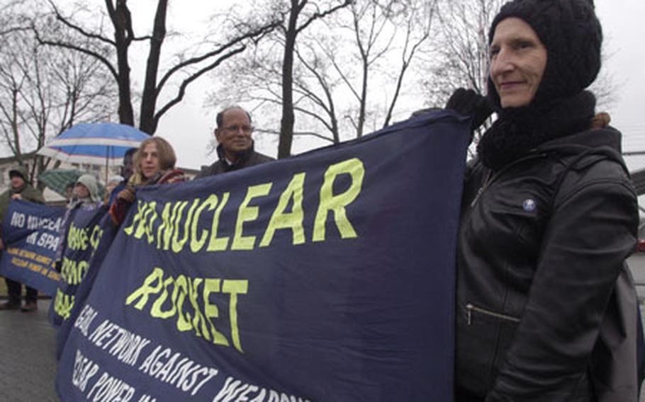 Linda Richards, an American and former Army brat who lives in Oregon, holds a banner Saturday at a rally outside the August-Euler Airfield in Griesheim, Germany. Richards, the daughter of a retired Army lieutenant colonel, was among more than 40 people who came from around the world to participate in a two-day conference and rally in Darmstadt and neighboring Griesheim to protest the militarization of space and U.S. spy bases in Europe.