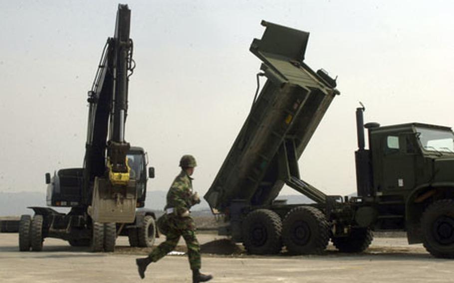 A sailor gets in position while machines fill a simulated large blast holes at a South Korean air base runway in Pohang Friday. Seabees from Naval Base Ventura County, Calif., worked with their South Korean counterparts on filling and covering the hole with a 3,000-pound fiberglass cover, trying to finish the task as quickly as possible while high-ranking officials observed.