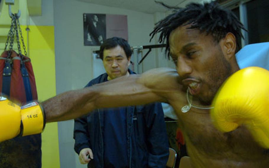 Professional kickboxer and former sailor Kevin Parker slams the sand bag Monday in anticipation of this weekend's Shin Nihon Kickboxing fight while "sensei" Yoshihiko Watanabe counts off punches.