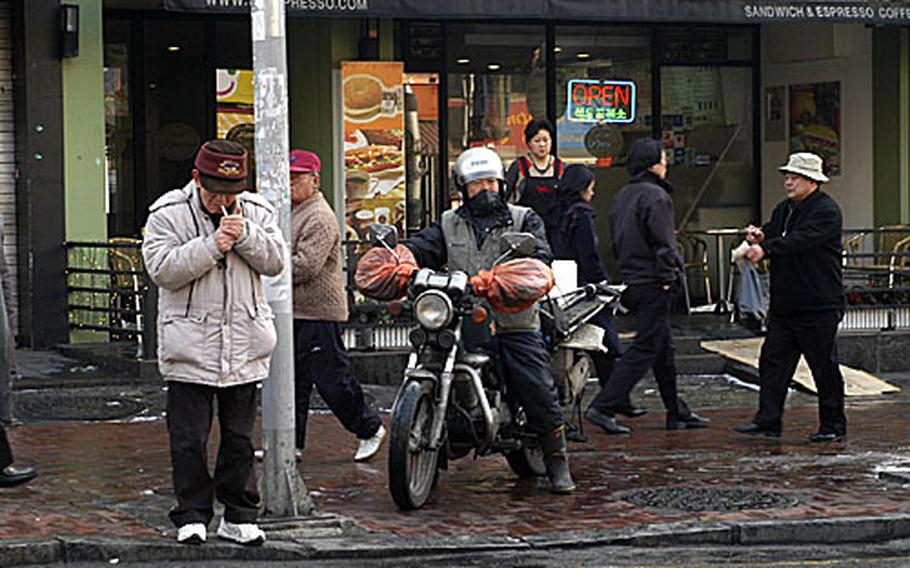 A motorcyclist waits on the sidewalk with pedestrians in Seoul.