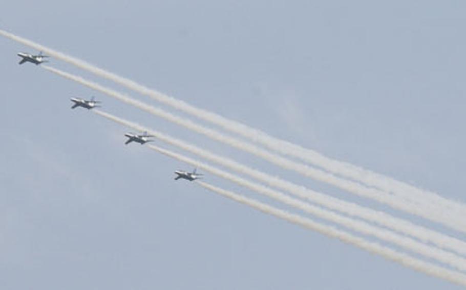 The Japan Air Self–Defense Force’s Blue Impulse aerobatics flight demonstration team flies overhead.