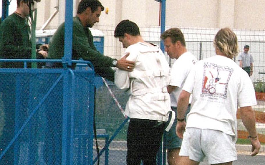 Petty Officer 1st Class Jonathan Edmiston — buckled, bound and ready for flight — is assisted onto the crane lift for a bungee-jump straitjacket escape in England in 1997.