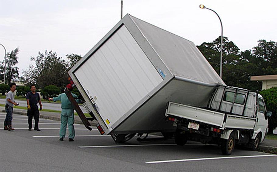 Workers on Kadena Air Base examine a van that toppled into a pickup truck by the strong winds of Typhoon Man-yi Friday in the commissary parking lot.