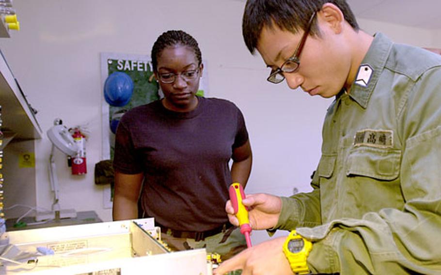 Senior Airman Alysha Landers, 21, from Columbus, Ga., a ground radio operator with 18th Communications Squadron, watches Wednesday as Japan Air Self-Defense Force Staff Sgt. Yuki Takasaki, 21, a ground radio operator from Okinoerabu-Jima Air Station, works on a radio at Kadena Air Base, Okinawa. Takasaki was at Kadena working with Landers for a week as part of Kadena's Bilateral Exchange Program.