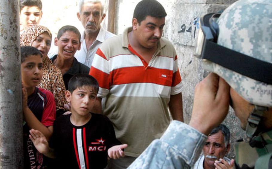 An interpreter working with U.S. troops wipes sweat from his brow while questioning a group of Iraqis in the Al Farouk neighborhood of Mosul.