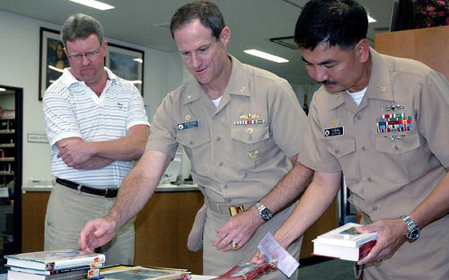 Command Master Chief Marcos Sibal, right, looks over new books last year at the Sasebo Naval Base, Japan, library with librarian Wayne Newman, left, and Fleet Activities Sasebo commander Capt. Tilghman Payne. Sibal will report in mid-August for duty as the new command master chief of the Navy’s 7th Fleet.