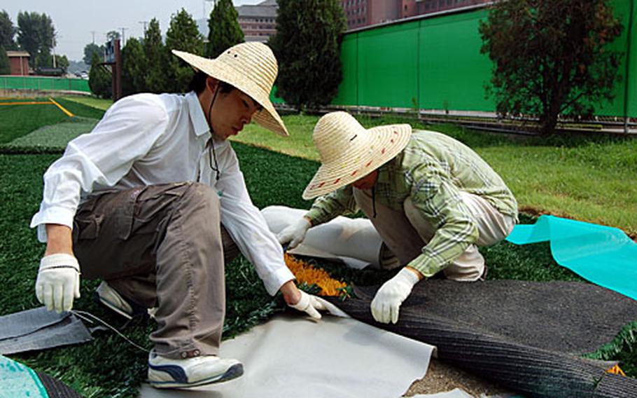 Lee Gu-yup, left, and Park Byong-gu place artificial turf on Falcon Field at Yongsan Garrison.