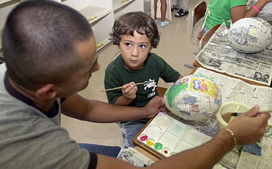 Six-year-old Ken Stone listens as Petty Officer 2nd Class Duran Garcia describes the colors the two could use to paint their papier-mache pinata Thursday at the AmerAsian School in Ginowan City. Garcia and other sailors with from Commander Fleet Activity Okinawa volunteer once or twice a week during the school's summer program.