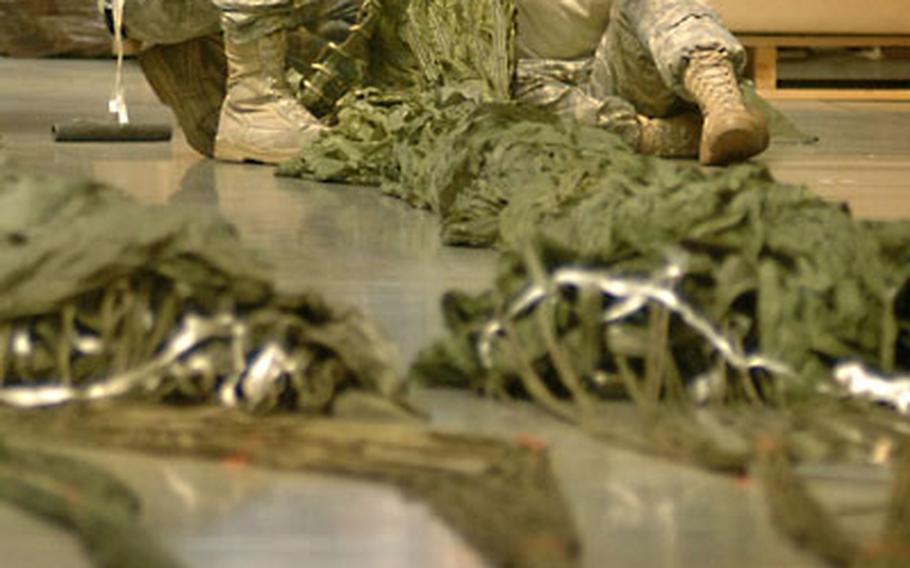 Spc. Dion Gutierrez and Sgt. Kathryn Johns, Army National Guard soldiers from the 128th Quartermaster Company (Air Drop Light), patch holes made in cargo chutes Tuesday at the Miesau Ammunition Depot, Germany. The reworked chutes that have been shelved since 1994 will be put back into operational use.