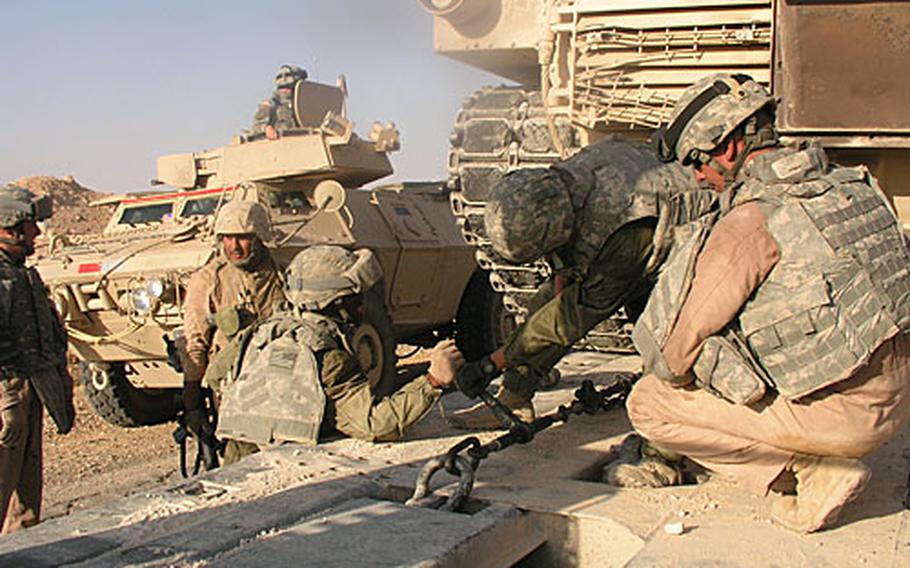Soldiers of the 25th Transportation Company, 787th Combat Sustainment Support Battalion, work vigorously in the intense heat Thursday to secure a U.S. Marine Corps tank to a trailer so their convoy can resume its trip from Combat Outpost Rawah to Al Asad Air Base in western Anbar province in Iraq. Two tires went out on the trailer the tank had initially been secured to, so convoy leaders switched it to an undamaged trailer.