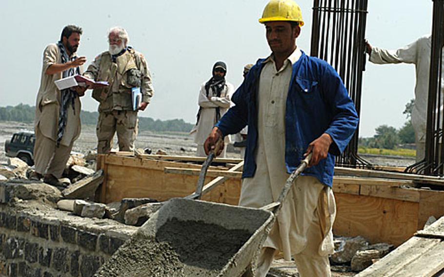 An Afghan worker pushes a wheelbarrow away from the Dadwal Bridge in Khost province while U.S. Army Corps of Engineer liaison Michael Butler discusses progress on the bridge with the Turkish contractor supervising the project.