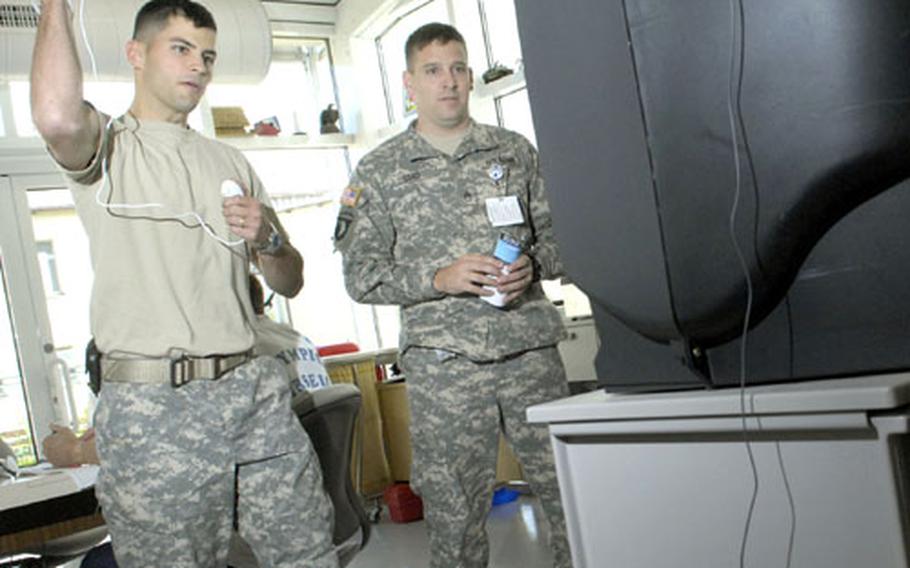 Army 2nd Lt. James Lakey, from the Center for Health Promotion and Preventive Medicine-Europe, uses a special wireless controller that interfaces with the Nintendo Wii to exercise an injury as Army Staff Sgt. Jason Lord, the noncommissioned officer in charge of the occupational therapy clinic, looks on Tuesday at Landstuhl Regional Medical Center.