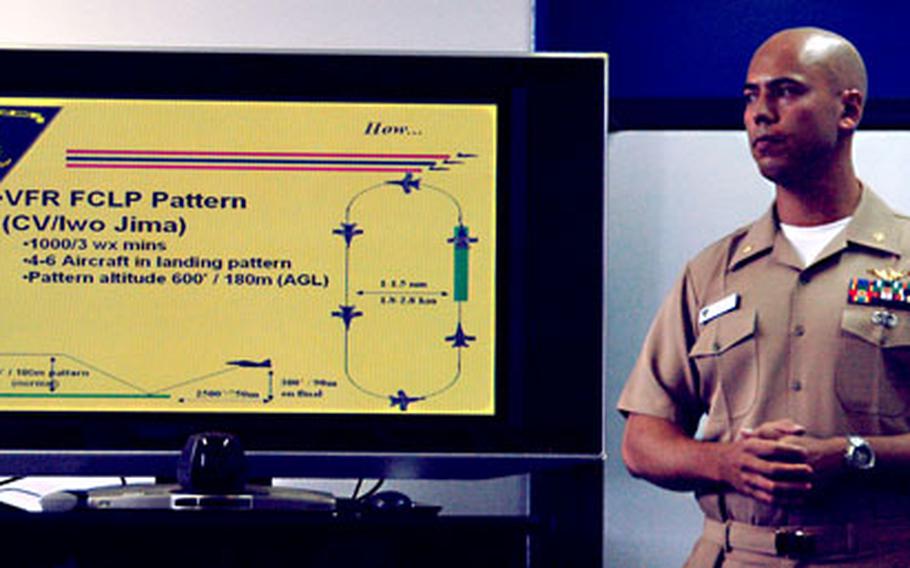 Lt. Cmdr. Erik Odom, a Carrier Air Wing 5 landing signal officer, briefs members of the Japanese press corps on field carrier landing practices prior to the media being treated to some flying time in the Navy’s F/A-18 flight simulators at Naval Air Facility Atsugi, Japan.