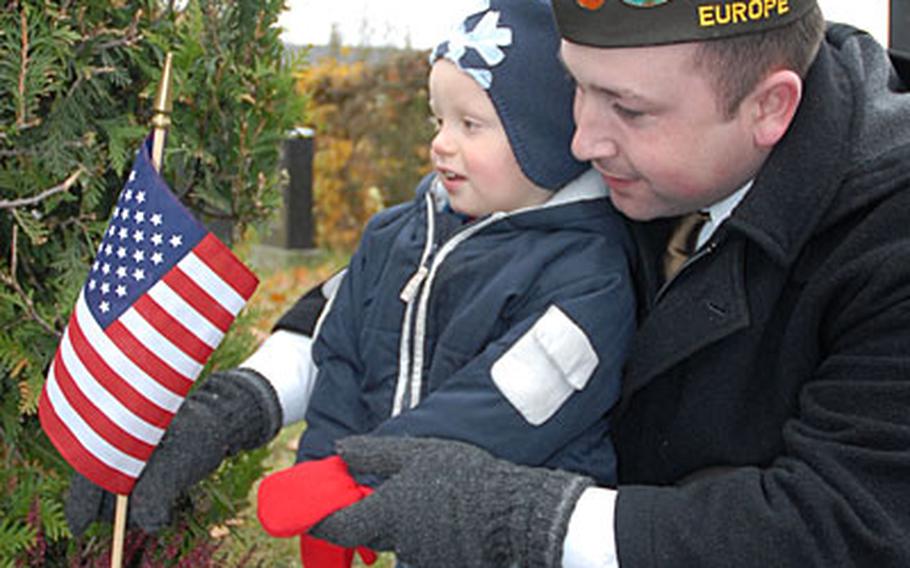 In honor of Veterans Day, Travis Fosmo, a member of Veterans of Foreign Wars of the United States Richard E. Austin Post 10592, and his son Fabian, 2, replace a flag at the grave of an American serviceman at a cemetery in downtown Bamberg, Germany.