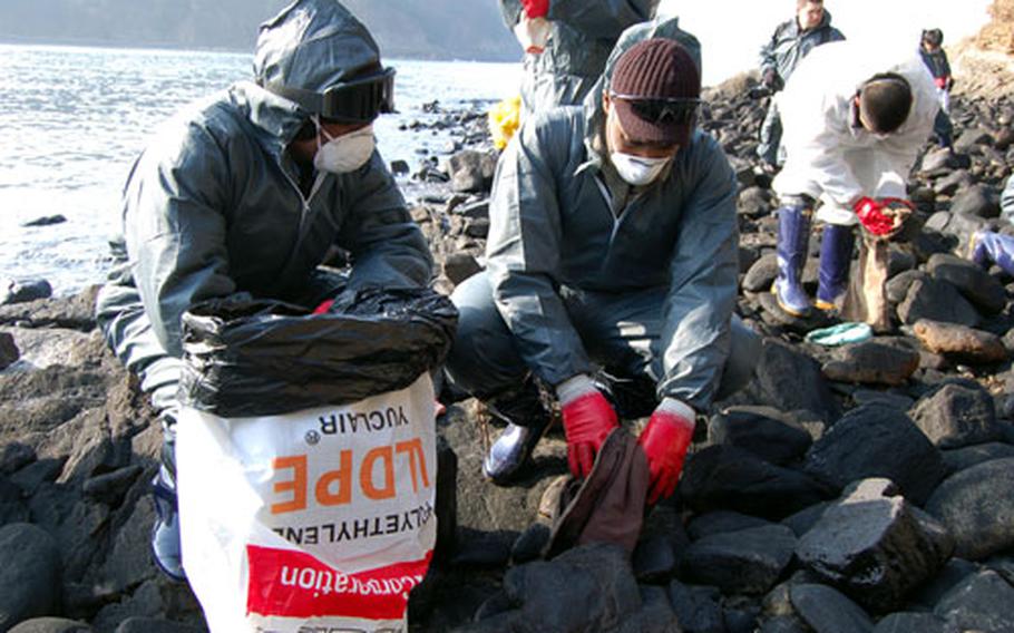 Staff Sgt. Anthquian Brummitt, right, and Staff Sgt. Billy Swanigan, both of the United Nations Command Honor Guard, scrub the oil from rocks on Baeknipo Beach on Wednesday as part of a U.S. military volunteer effort to help clean up a Dec. 7 oil spill.