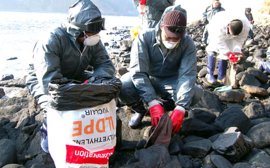 Staff Sgt. Anthquian Brunnitt, right, and Staff Sgt. Billy Swanigan, both of the United Nations Command Honor Guard, scrub the oil from rocks on Baeknipo Beach on Dec. 19. An 8th Army spokesman confirmed Thursday that none of the roughly 200 U.S. troops who volunteered to assist with the clean-up have reported any illnesses relating to their on-site work.