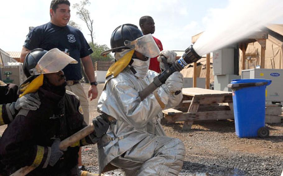Instructor Alex Vinces, middle, and fire chief Desi Wade, back right, watch as firefighting recruits work with the fire hose during a training exercise Sunday on Camp Lemonier, Djibouti.