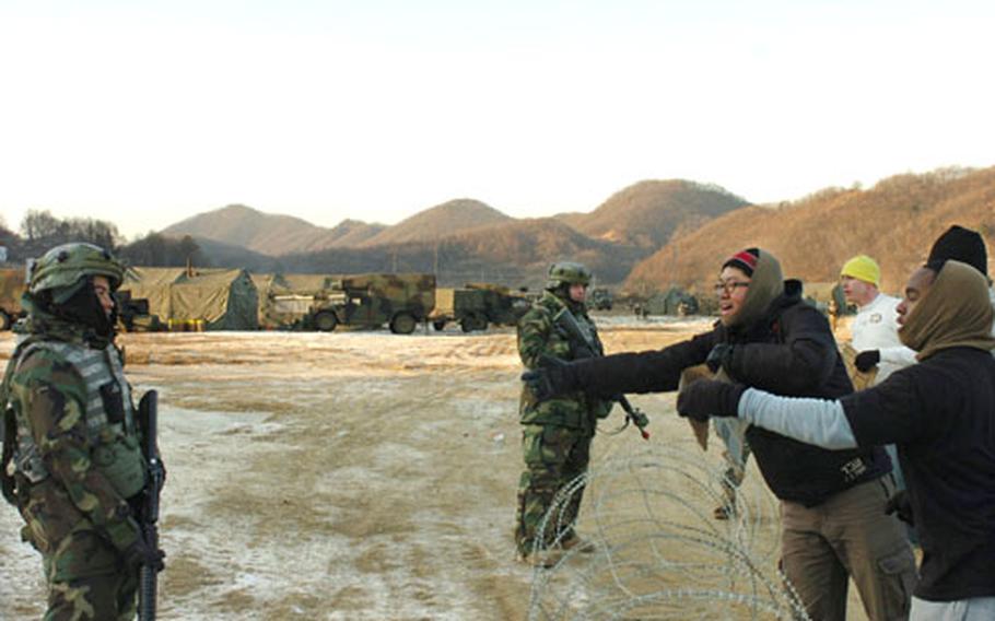 Clockwise: Pvt. Anurt Ablat and Spc. Gregory Gilbert stand guard as "protesters" Pfc. Jacob Chadwick, Pvt. Lee Jung-sung and Spc. Stephen Boone taunt the soldiers Wednesday at Twin Bridges training area.