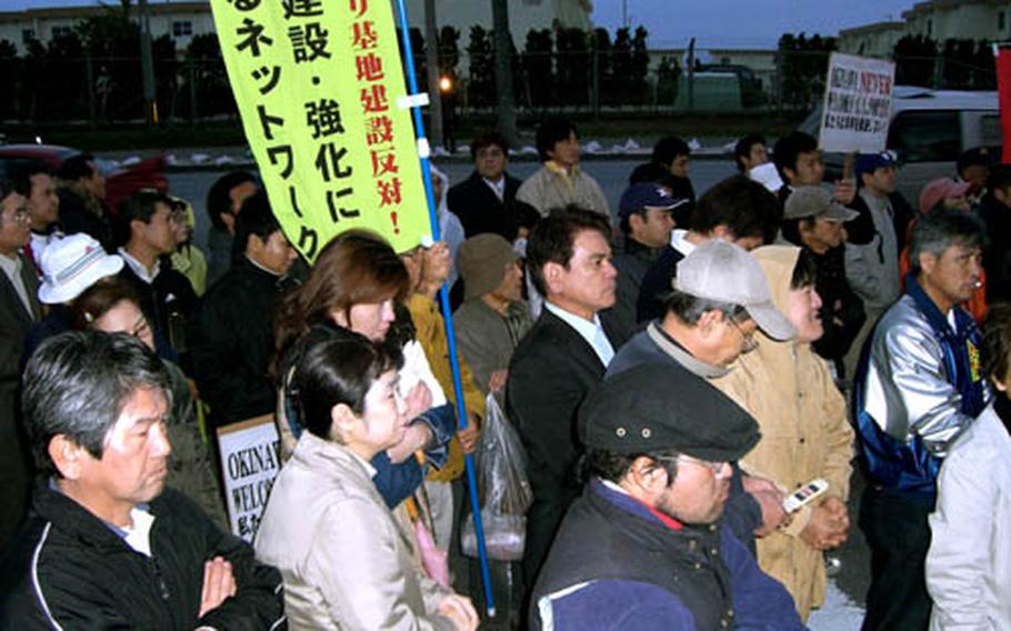 In this file photo from February 2008, demonstrators stand outside the Headquarters Gate of Camp Foster to protest the alleged rape of an Okinawan girl. The banner proclaims opposition to a new Marine Corps air facility planned for Camp Schwab to replace Marine Corps Air Station Futenma. The white sign at right reads, 'Okinawa never welcomes U.S. forces.'
