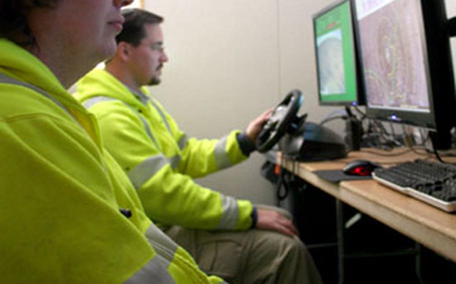 DARPA researchers Dan Tascione, front, and Mike Sergi-Curfman drive the crusher remotely Feb. 19 from their command center at Fort Bliss, Texas. The two adapted video game controllers to steer the massive vehicle and operate its cameras.