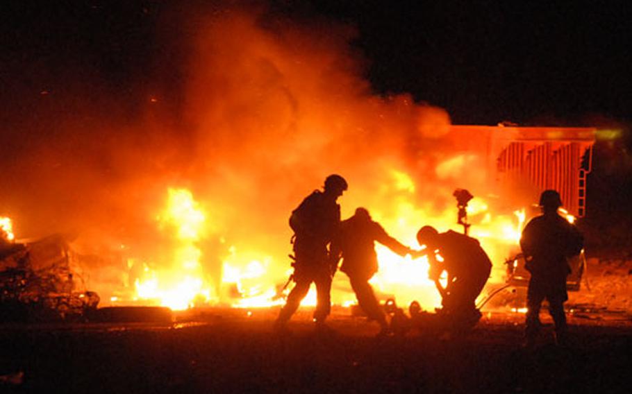 Iraqi and American soldiers haul away a bomb squad robot after a pickup truck exploded while the robot was searching it. The robot was able to limp along under its own power once the soldiers set it down on the road.