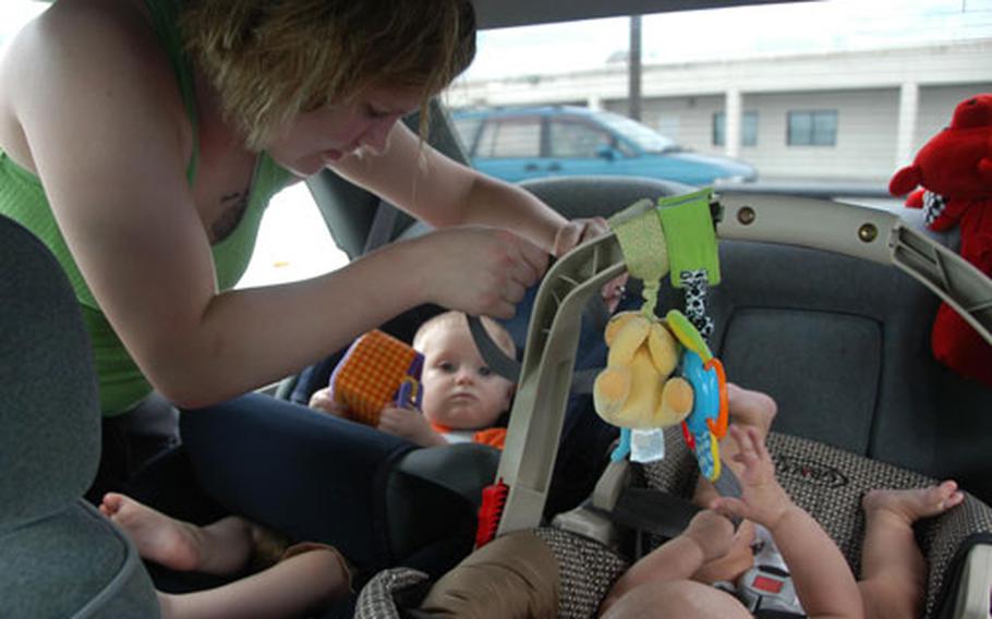 Elizabeth Dickson, left, helps snap in the baby carrier of her friend’s five-month-old daughter, Nasiah Mimms, center, after shopping at the Kadena exchange Monday. Her son, Chandler, 10 months, is ready to ride. Although military bases require all passengers to buckle up on base, a new Japanese law now requires back seat passengers to wear seat belts in town.