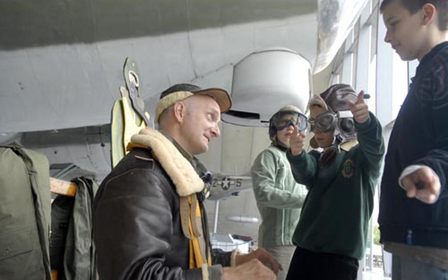 Stephen Wisdom, a docent at the American Air Museum in Duxford, shows children the uniform and gear used by pilots during World War II.