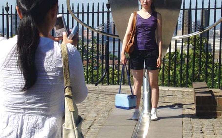 A visitor to the Royal Observatory has her photo taken as she straddles a metal line representing the prime meridian, with one foot in the Eastern Hemisphere and the other in the Western Hemisphere.