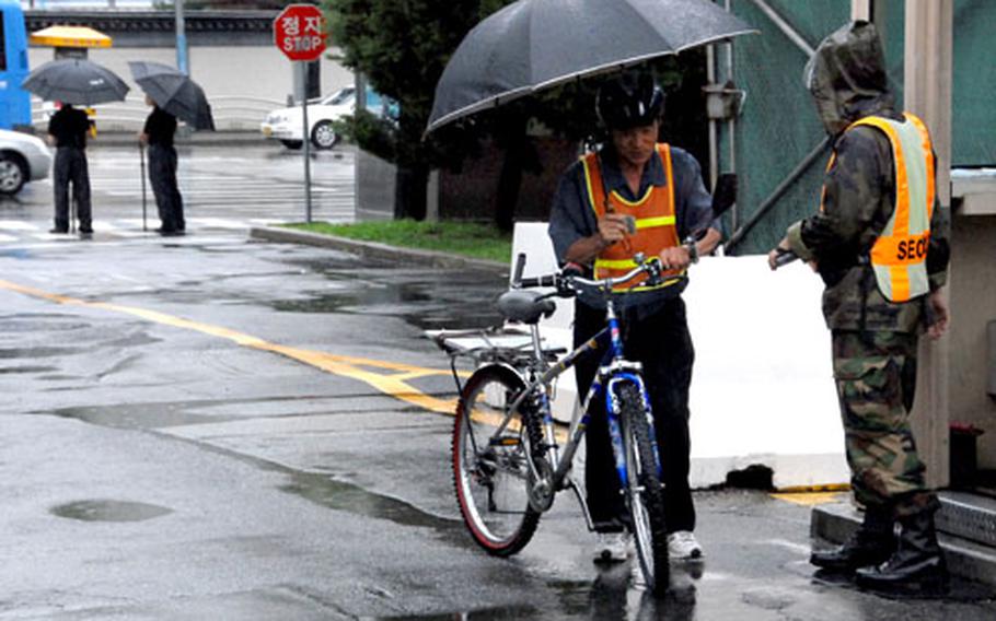 A South Korean man tries to stay dry on Thursday as he gets his identification card scanned before entering U.S. Army Garrison-Yongsan.