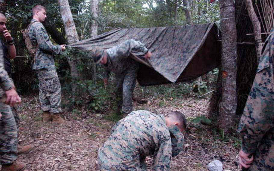 Marines from the 3rd Fleet Anti-terrorism Security Team, 1st Platoon build a tent using a poncho and tree limbs they cut down during survival training Tuesday at the Jungle Warfare Center on Okinawa. The poncho shelter is one of the quickest shelters to assemble.