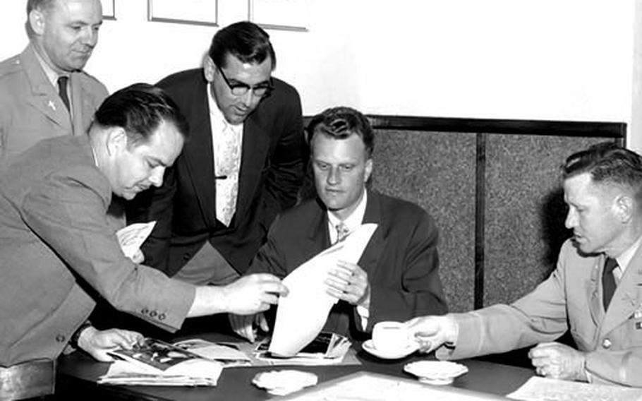 Rev. Billy Graham is shown some of the day's news photos during the evangelist's visit to the newspaper's production facility in Griesheim, Germany, in 1955.