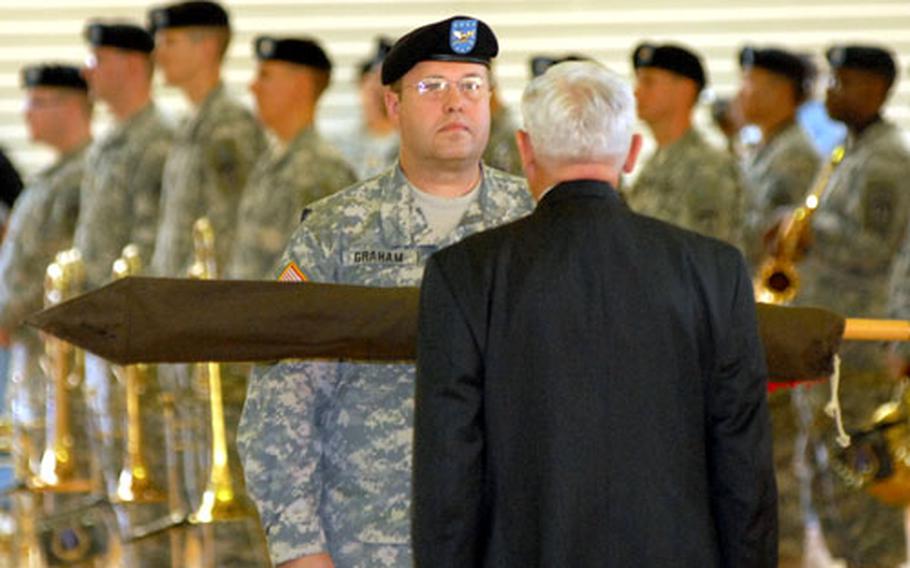The colors of U.S. Army Garrison Hessen were cased on Wednesday by garrison commander Col. Ray Graham, left, and Robert Schloesser, deputy to the commander, in a ceremony on Pioneer Kaserne in Hanau, Germany, on Thursday. In the background is the USAREUR Band, which provided the music for the ceremony.