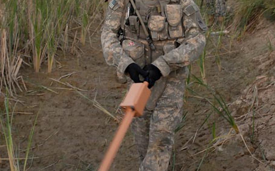 Spc. Tiburcio Bazante sweeps a mine detector through a muddy canal Friday during a search for weapons caches near Al Batta, Iraq.