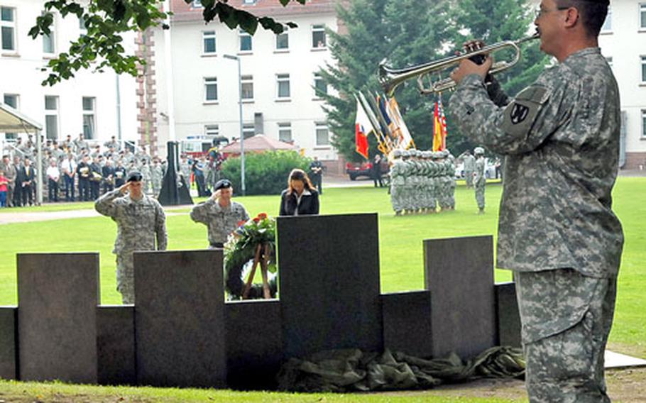 Spc. George Weber of the 76th Army Band plays taps at a memorial dedication ceremony for the fallen of the 21st Theater Sustainment Command, as Sgt. Jason Strickland, Maj. Gen. Yves Fontaine salute and Kaiserslautern mayor Susanne Wimmer-Leonhardt bows her head.
