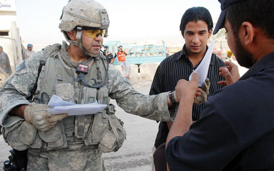 Staff Sgt. Gabriel Minor hands a wanted poster to an Iraqi man during a patrol Sunday in Jihad area. "Sons of Iraq" groups give intelligence tips directly to Company E, but leaders hope the transition to Iraqi government authority will help them work closer with Iraqi Army leaders.