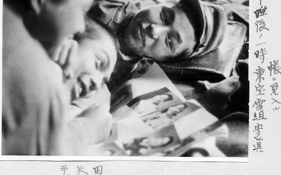 The writing on the photo reads: 1 p.m., second lieutenants Tanaka (right), Yano (center) and Tetsuka (left) look at a photo album of Toho Hana-gumi, a musical singer and dancer performing at Toho, a music hall at the central Ginza district in Tokyo.