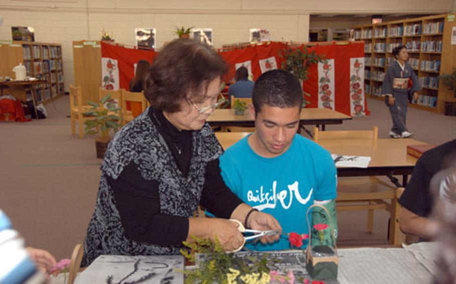 Instructor Sachiko Takaesu helps senior Danny Fisher, 17, cut carnations for a flower arrangement Thursday at Kubasaki High School. Fisher and classmates from his sociology class were learning Japanese flower arrangement, or ikebana, as part of a cultural activity day.