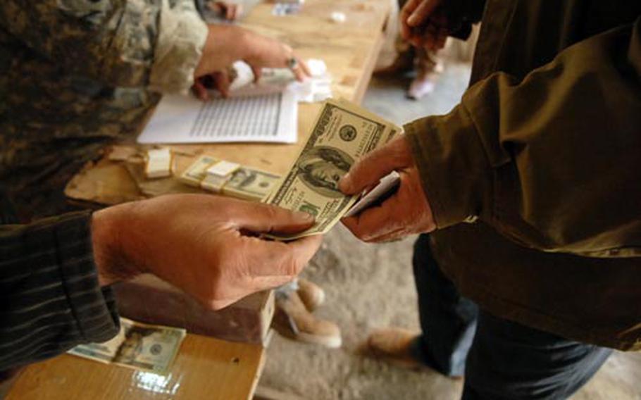 Salim Malah al-Saadi (left), a Community Project Workers supervisor, pays one of his workers Monday at a patrol base on the border of Baghdad’s Sadr City district.