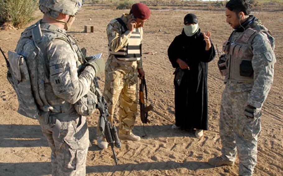 An Iraqi Army officer, along with Capt. Tom Smith and his interpreter, questions a woman during a raid Thursday on a farm that was believed to be harboring an al Qaida operative. The raid produced no captures despite evidence the wanted man had recently been on the property.