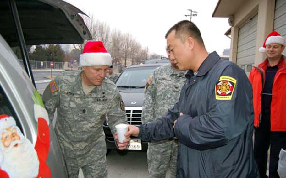 U.S. Army Garrison Yongsan Command Sgt. Maj. Ralph Rusch hands a cup of hot cocoa to Yongsan firefighter Chong Song-uk on Wednesday as part of Operation Santa Express, a 10-year garrison tradition in which officials bring treats to emergency services personnel.