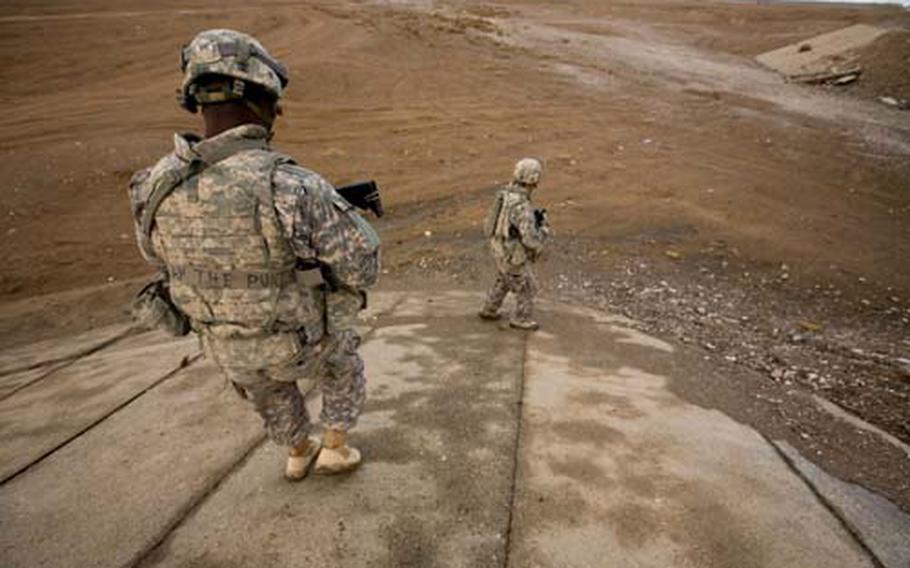 Spc. Christopher Kuntor, 26, of Accra, Ghana, and Sgt. Jeremiah Cummings, 28, of Charlotte, N.C., descend into a dry riverbed to check under a bridge for Taliban bombs in Maiwand district, Kandahar province, Afghanistan. The soldiers are with Destroyer Company, 2nd Battalion, 2nd Infantry Regiment.