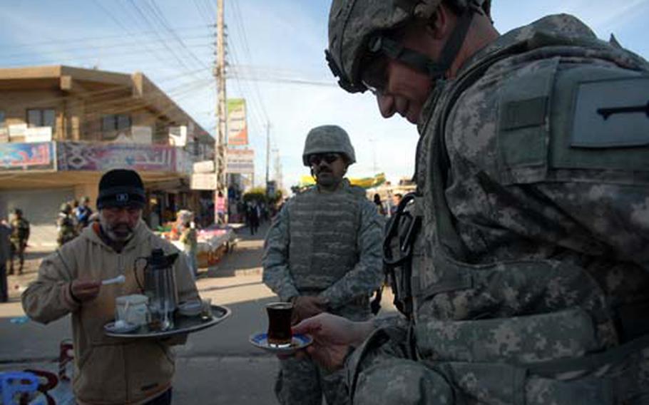 Col. Joseph Martin, commander of 2nd Heavy Brigade Combat Team, 1st Infantry Division, drinks a cup of tea offered by a local store owner Thursday during a patrol through Baghdad’s Amariyah neighborhood. Martin says his brigade is already busy helping to secure Iraq and that its duties won&#39;t change much for the election.