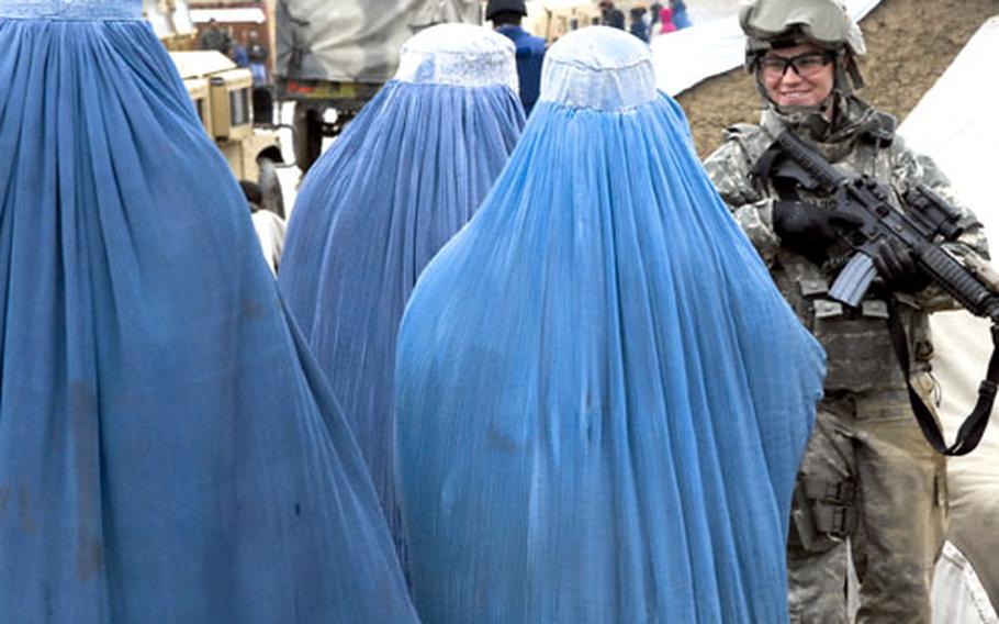 A member of the U.S. Army’s Police Mentor Team — Kabul smiles to passing women at a refugee camp in the capital. Though many women in Kabul wear Burqas, the dress code is far more relaxed than in rural parts of Afghanistan, and at least as many don’t.